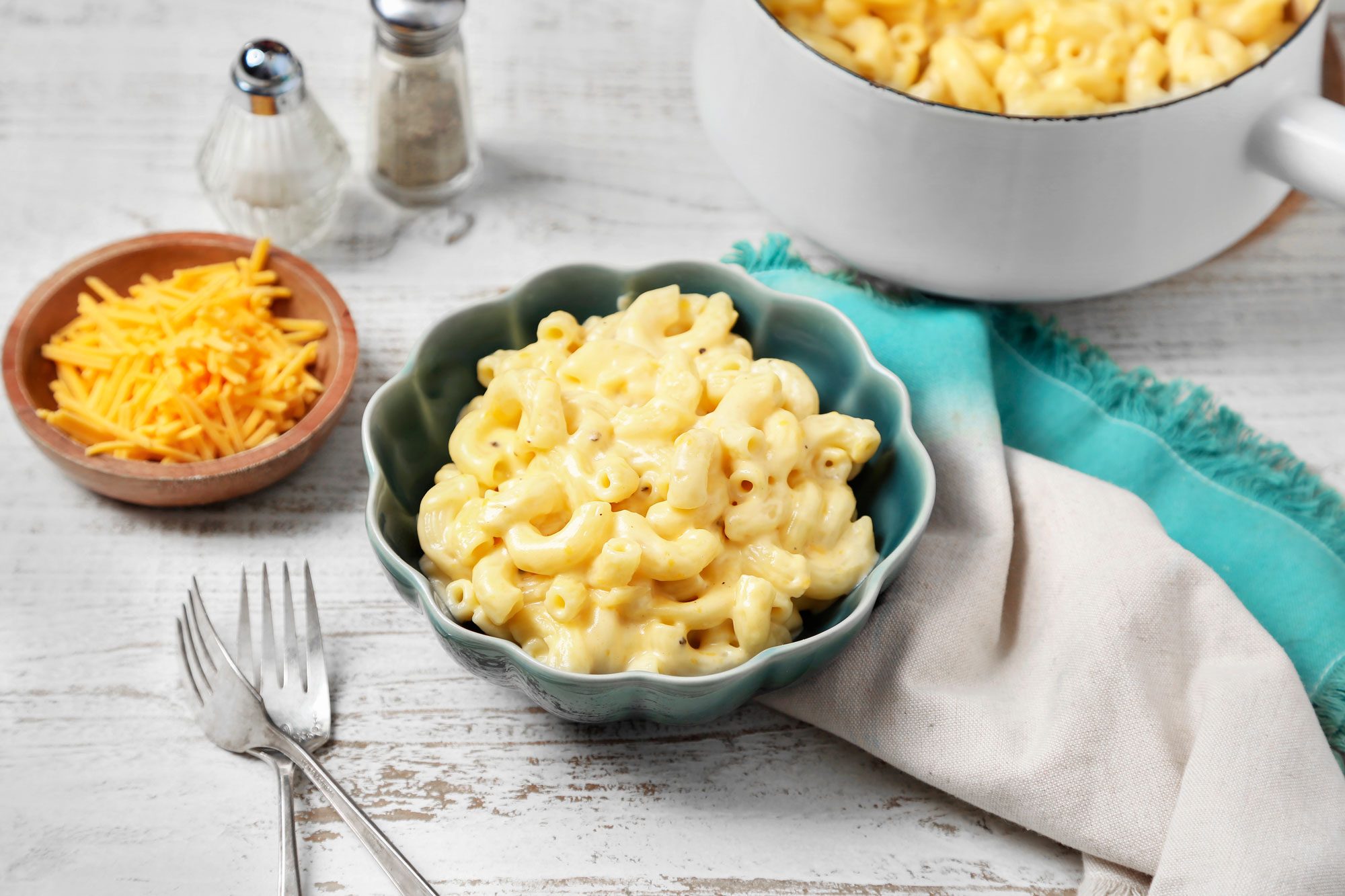 A plate of macaroni and cheese with a blue and white bowl and napkin on a white table