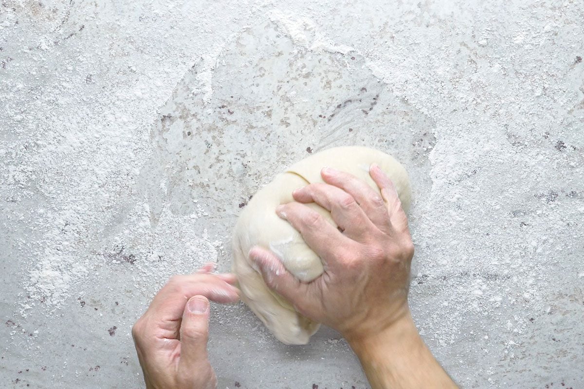 Overhead shot of turn dough onto a floured surface; knead until smooth and elastic 6-8 minutes; place in a greased bowl; turning once to grease the top; cover and let rise in a warm place until doubled; 1-1/2 to 2 hours; grey surface;