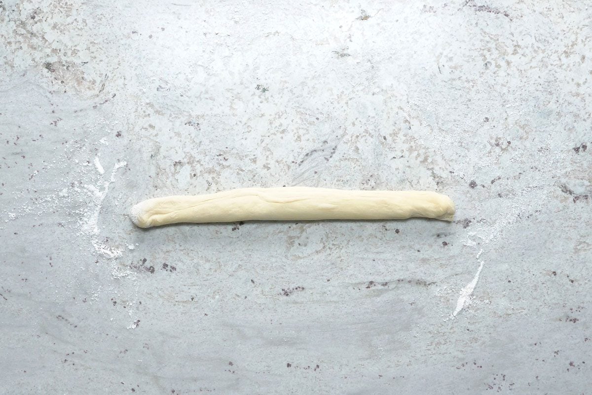 Overhead shot; punch down dough; Turn onto a lightly floured surface; divide into 6 portions; Roll each portion into a rope; grey surface;