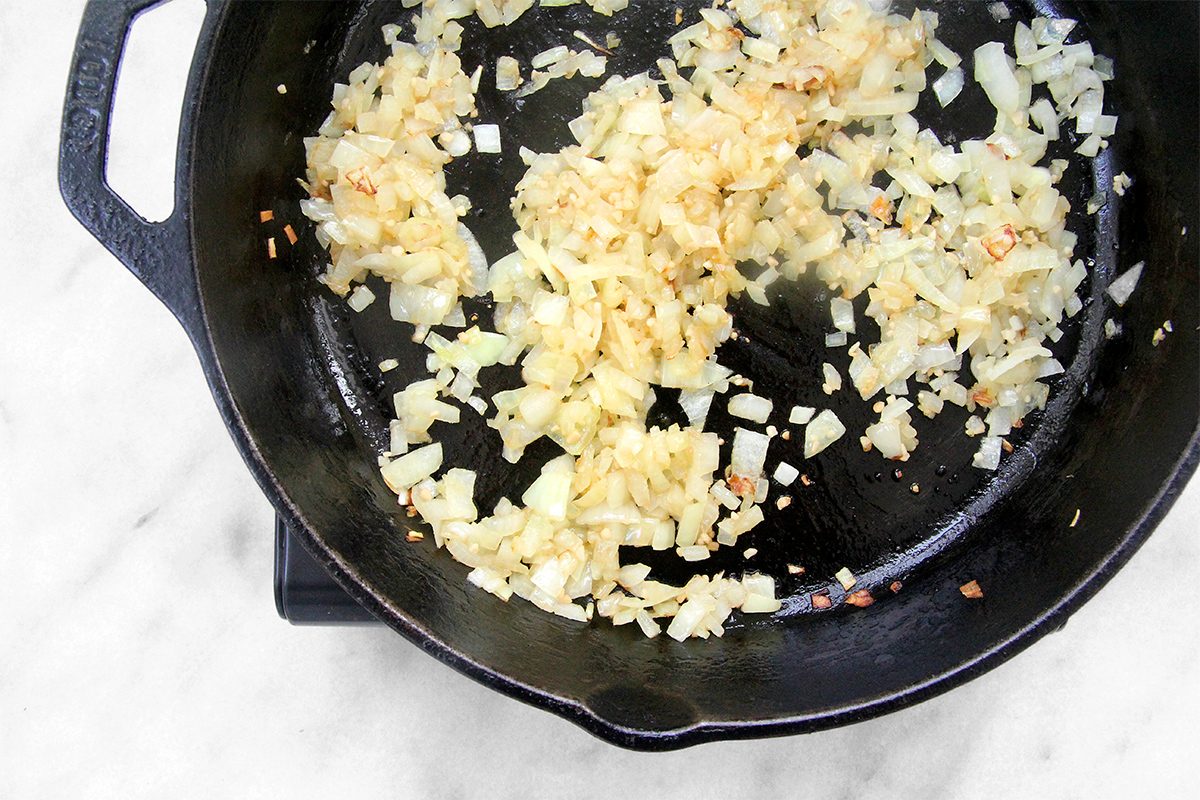 Chopped onions sizzling in a black cast iron skillet on a marble countertop.
