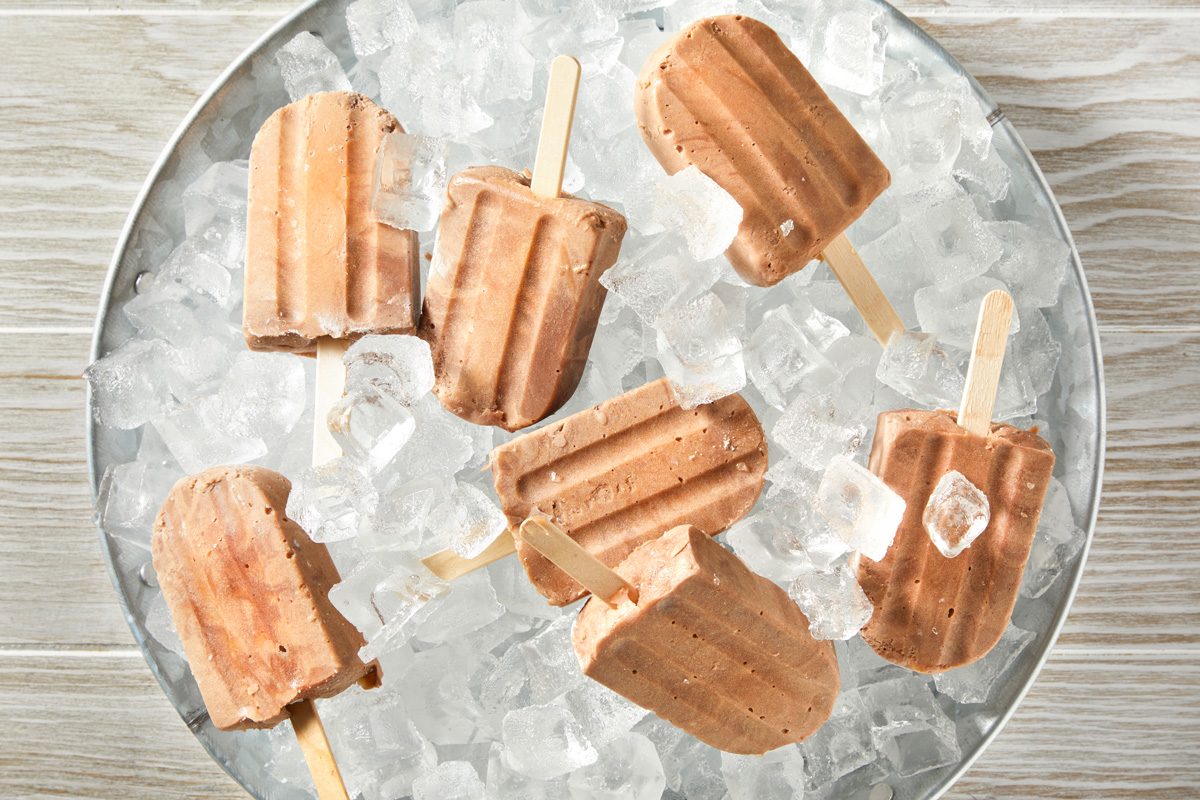 overhead shot of a close-up of a metal bowl filled with ice cubes and fudge pops; the bowl sits on a wooden table;