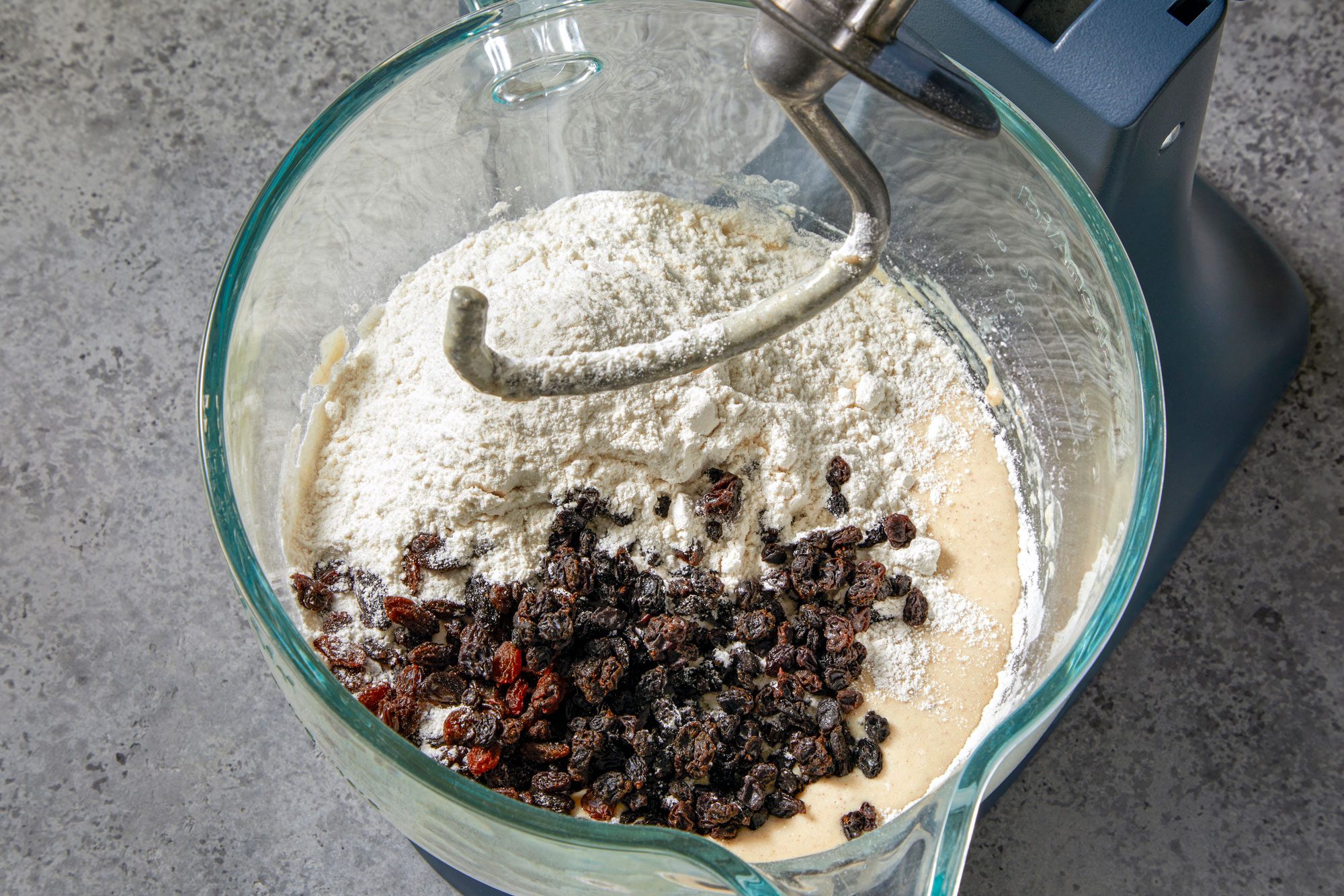 overhead shot of a glass bowl of a stand mixer is filled with ingredients for baking, the bowl is sitting on a gray countertop