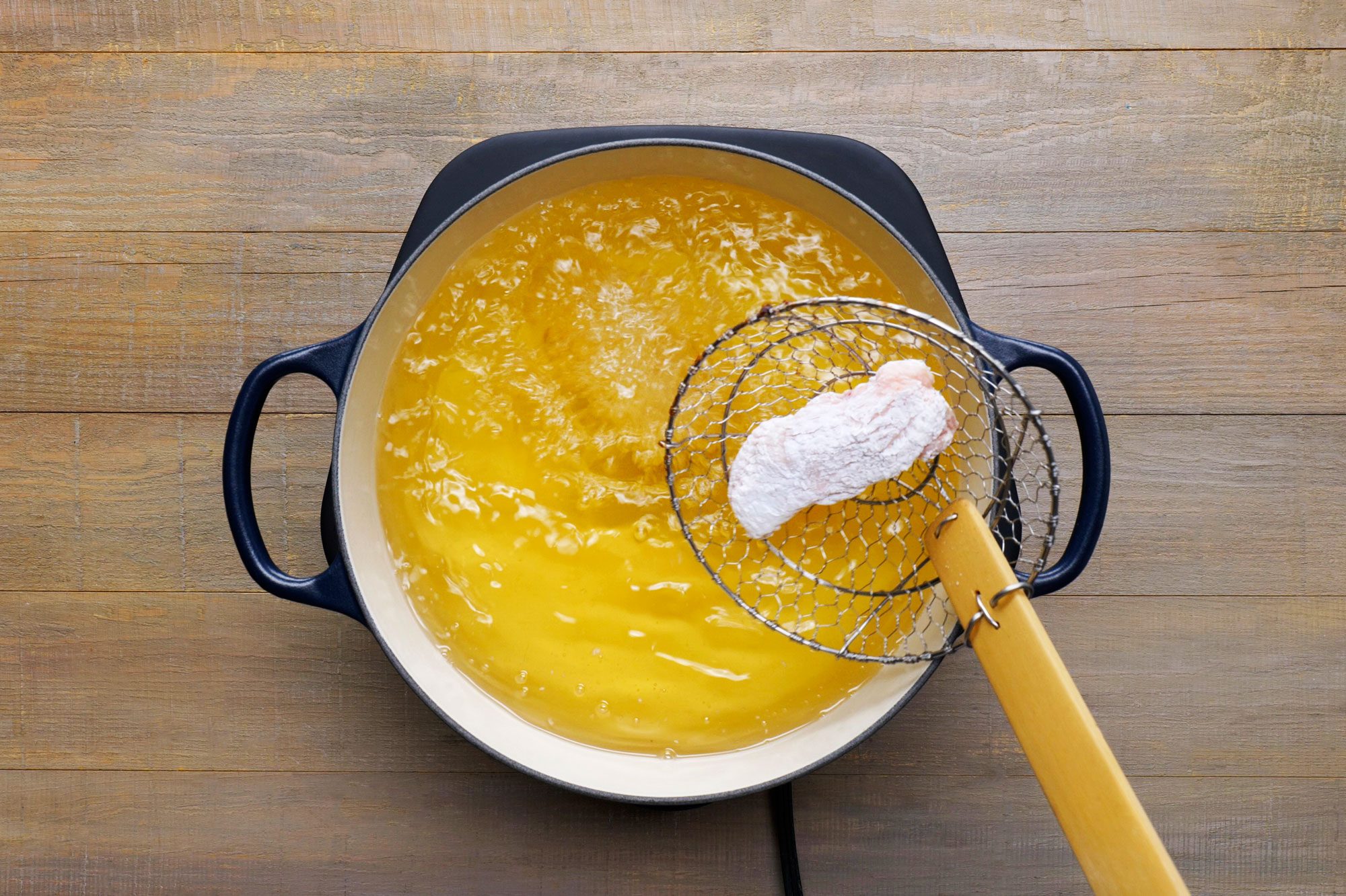 Deep frying flour coated wings in frying pan with hot oil