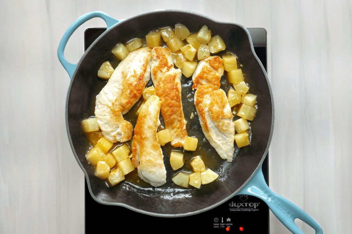 overhead shot of a blue cast iron skillet with chicken and pineapple cooking on an induction cooktop