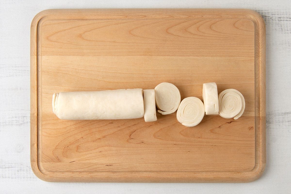 overhead shot of a wooden cutting board with a roll of dough that has been sliced into rounds