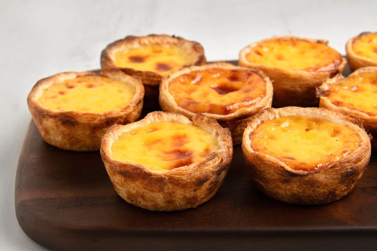 3/4th shot of Portuguese egg tarts, arranged on a wooden board; the background is a light gray