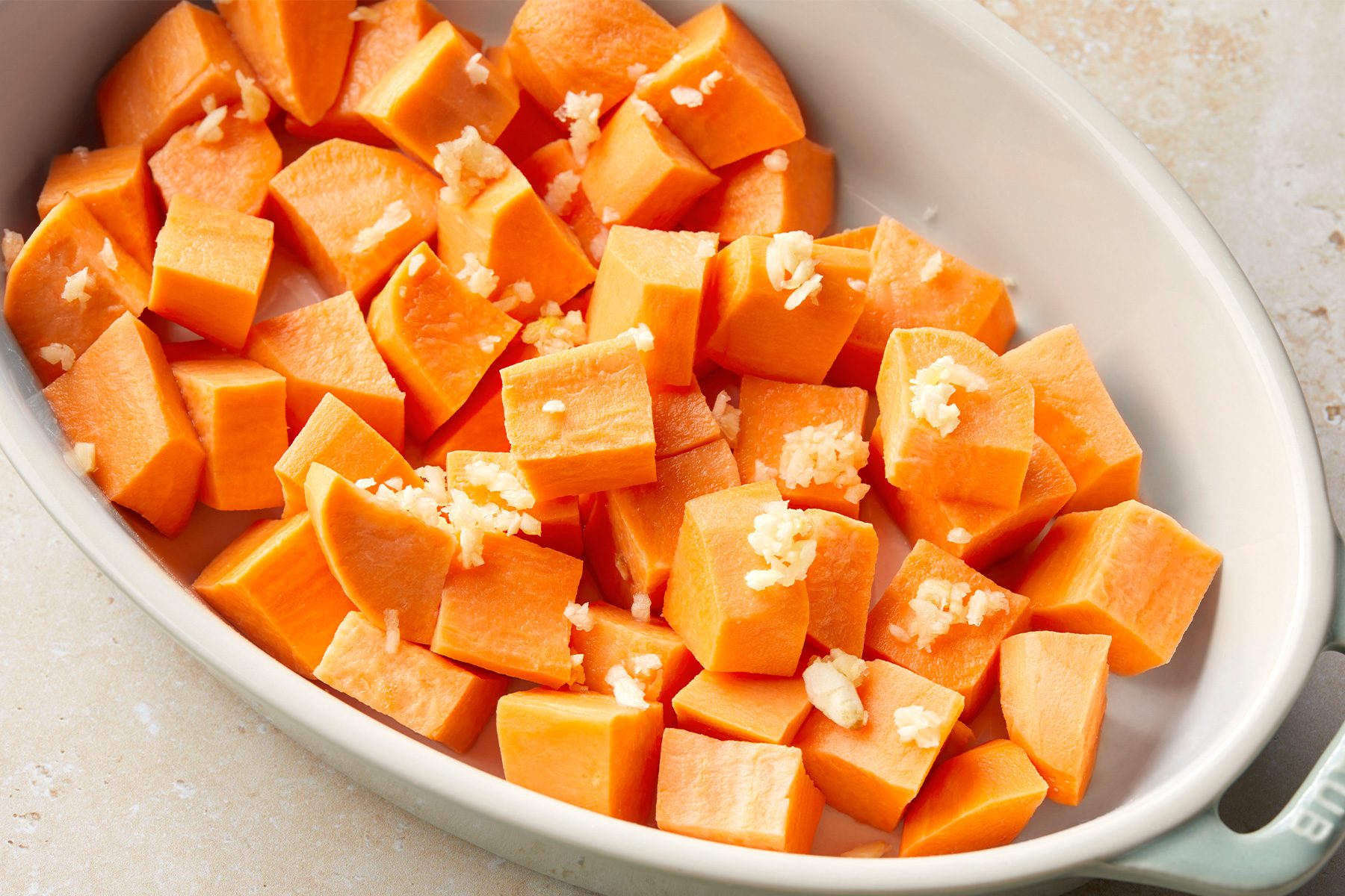 Sliced sweet potatoes in a bowl with sprinkled salt and garlic
