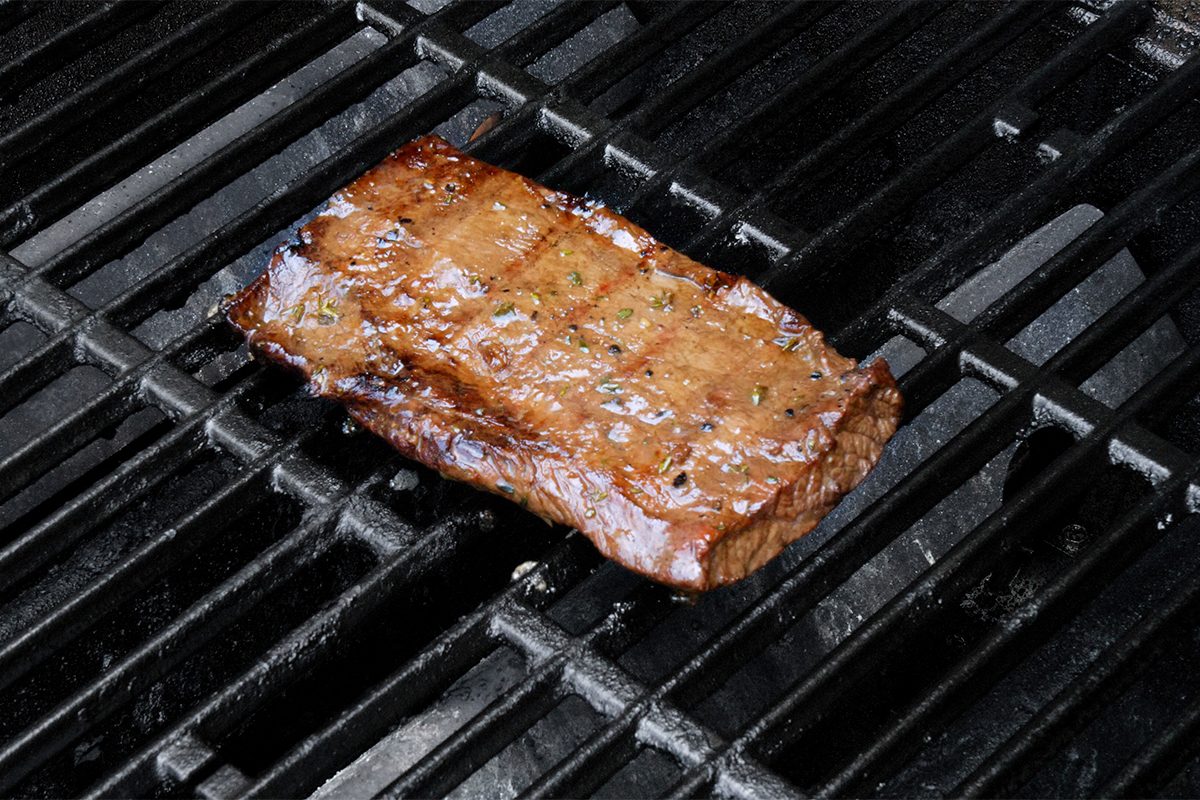 A marinated steak grilling on a black barbecue grill, showcasing grill marks and a glossy, cooked surface.
