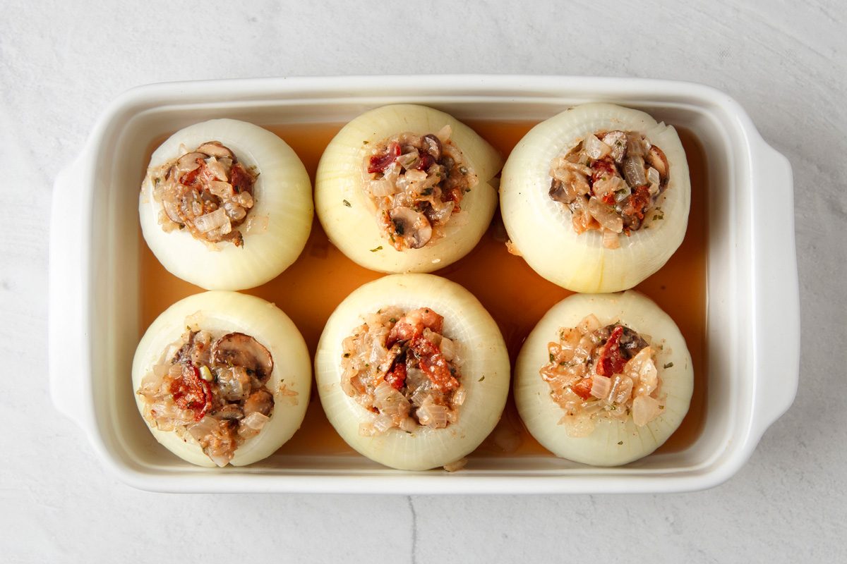 broth poured around filled onion shells in a shallow baking dish