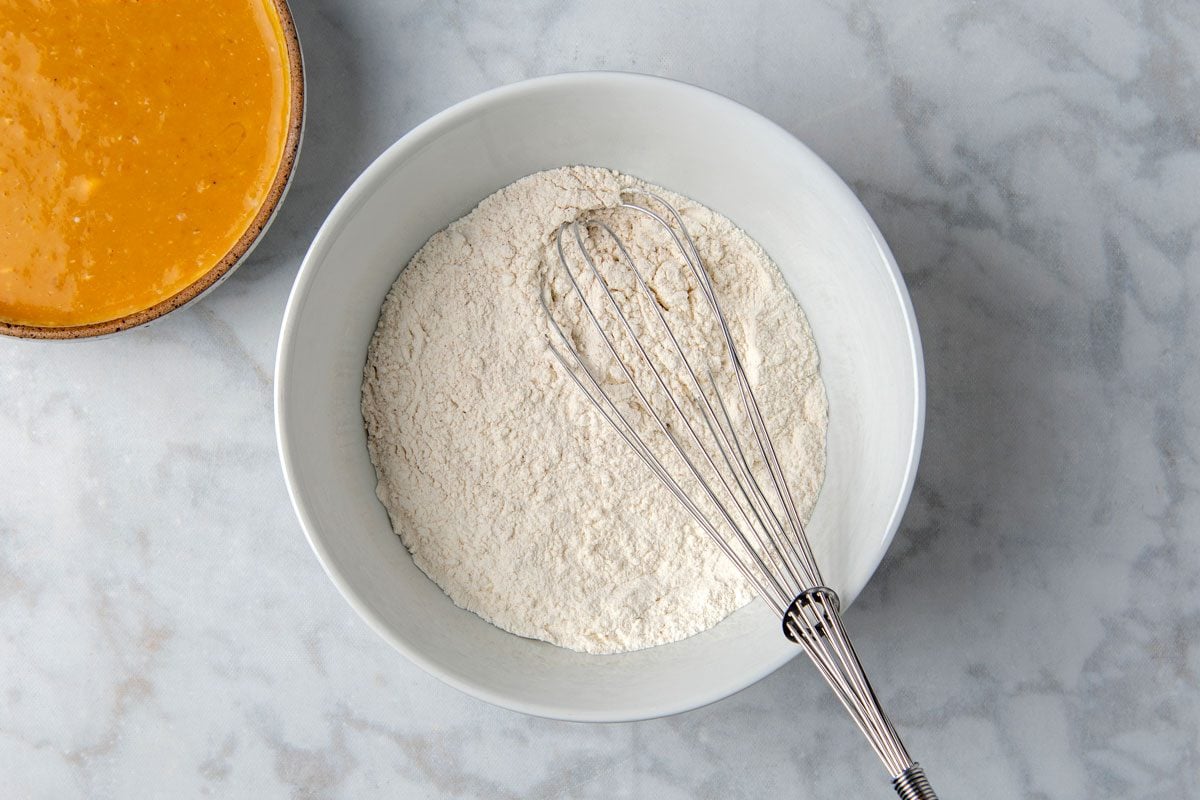 Overhead shot of a large bowl; whisk together first seven ingredients; In another bowl; combine sweet potato puree; milk; eggs; butter and vanilla extract until combined; whisk tool; marble surface;