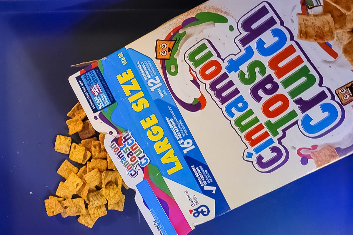Spilled box of Cinnamon Toast Crunch cereal on a blue surface. Box displays 