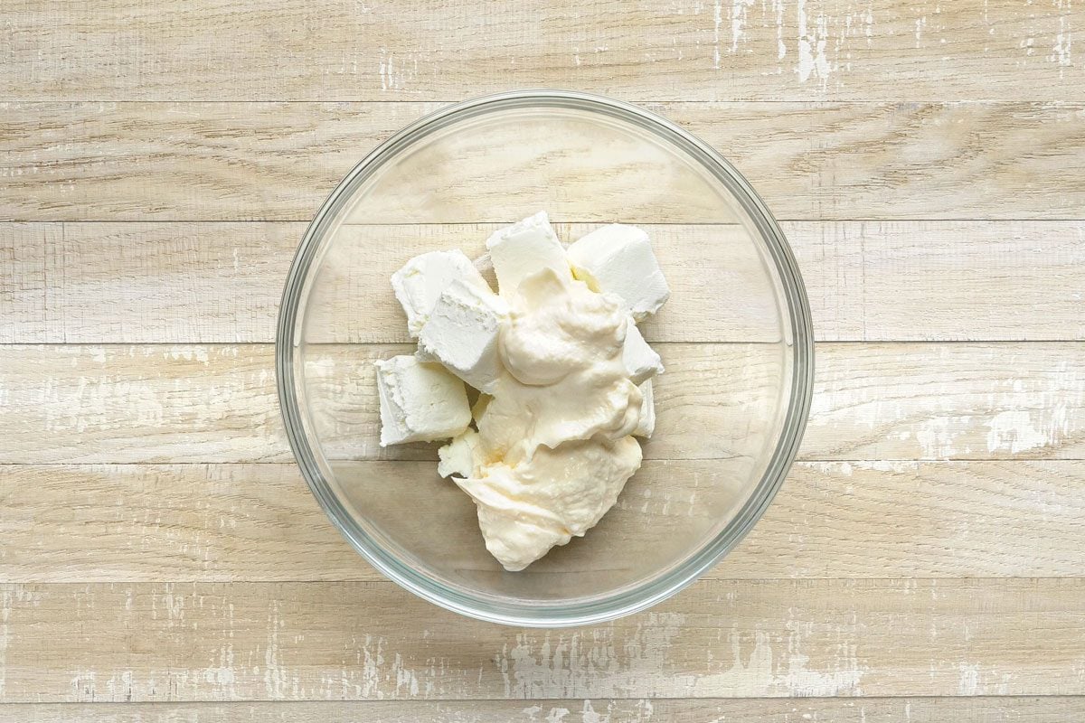 overhead shot of a glass bowl filled with cream cheese and mayonnaise, the bowl is sitting on a light brown wooden table