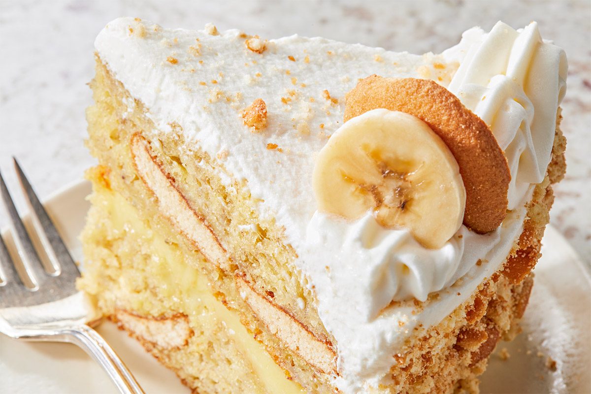 closeup shot of a slice of banana pudding cake, a fork sits beside the slice on a white plate