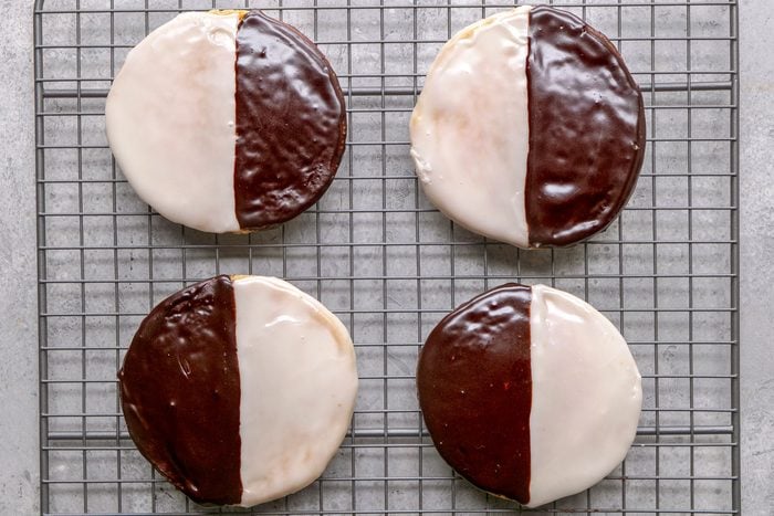 overhead shot of Four black and white cookies are arranged on a grey wire cooling rack, the background is a plain grey surface
