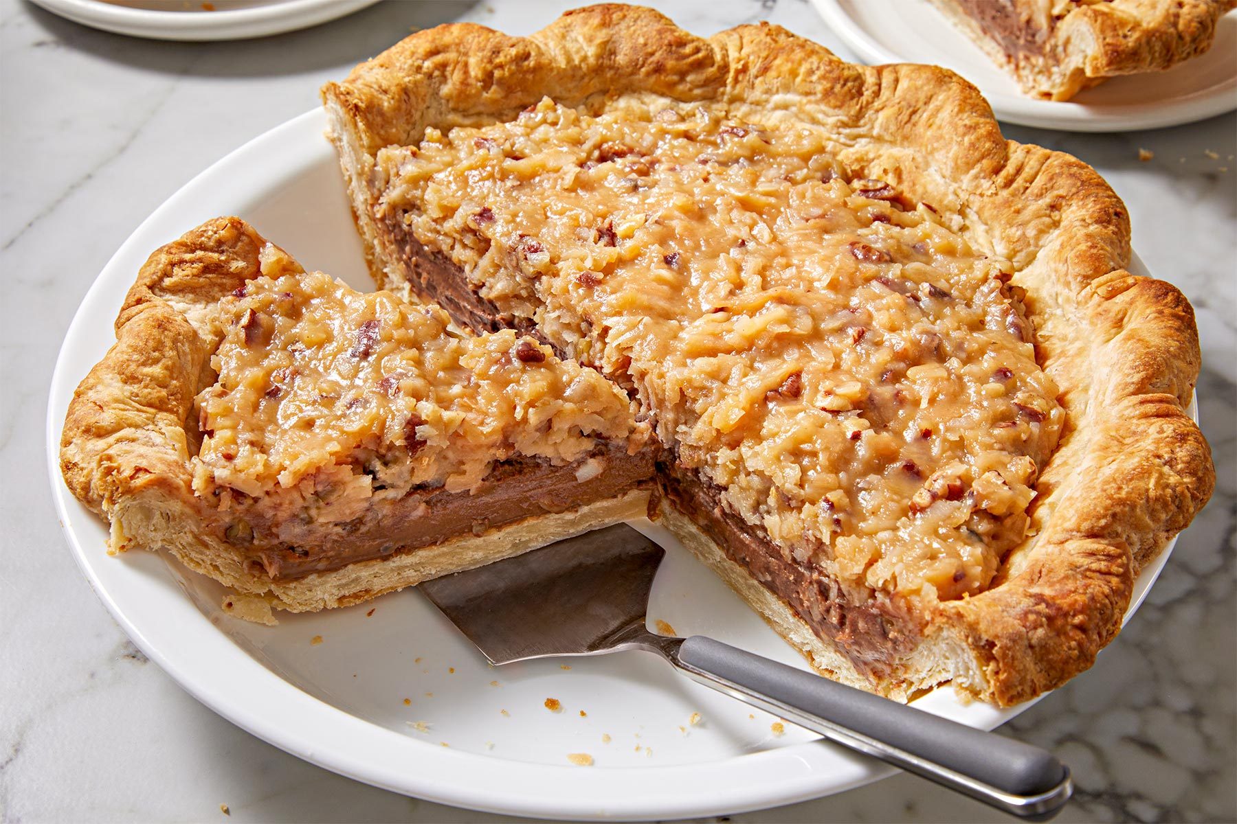 3/4th shot of German Chocolate Pie kept on a white plate with a serving spatula.