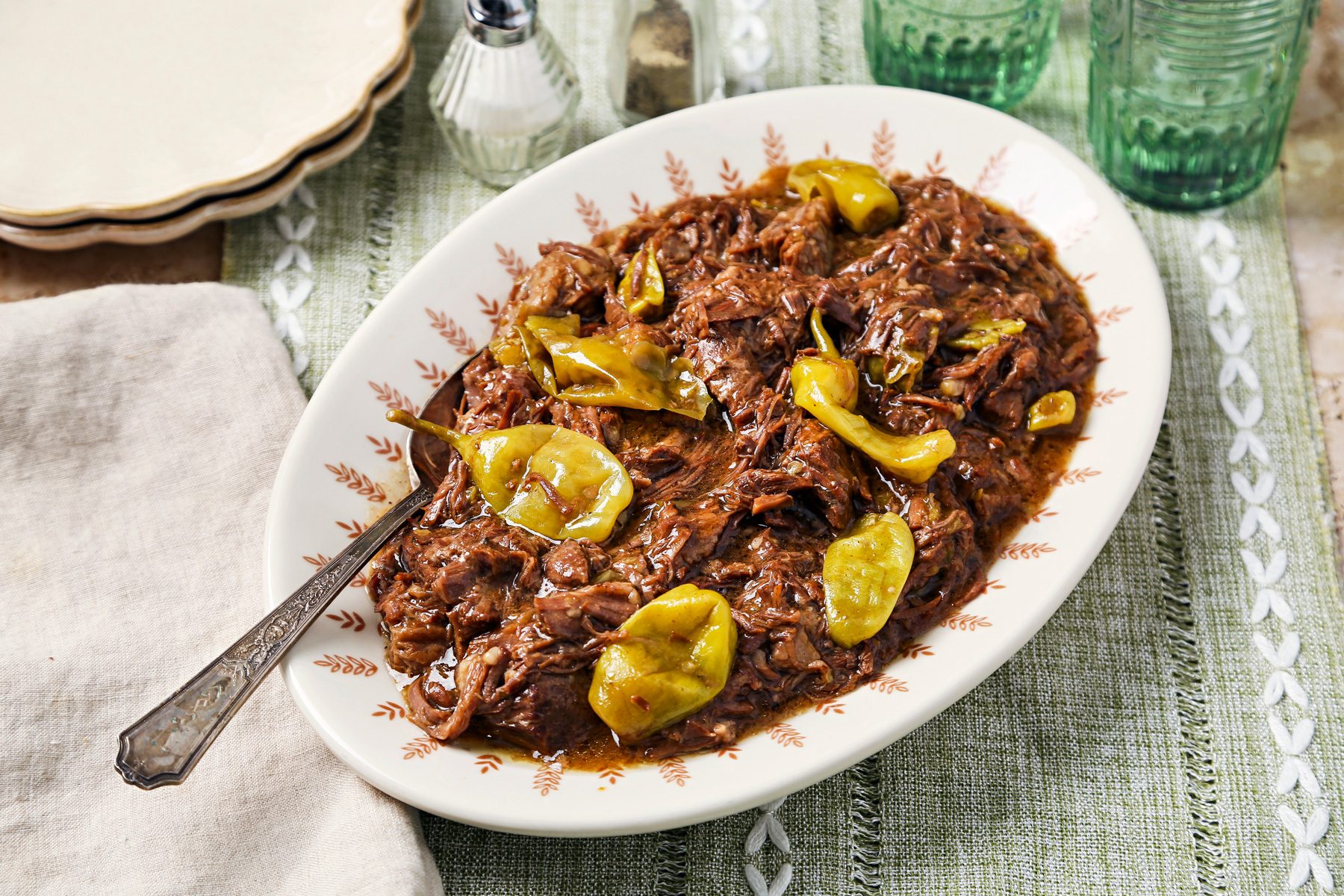 Cover push pull image of Taste of Home's Instant Pot Mississippi Pot Roast shot on a brown surface with a green linen. Pot roast shredded with peppers on a serving dish.