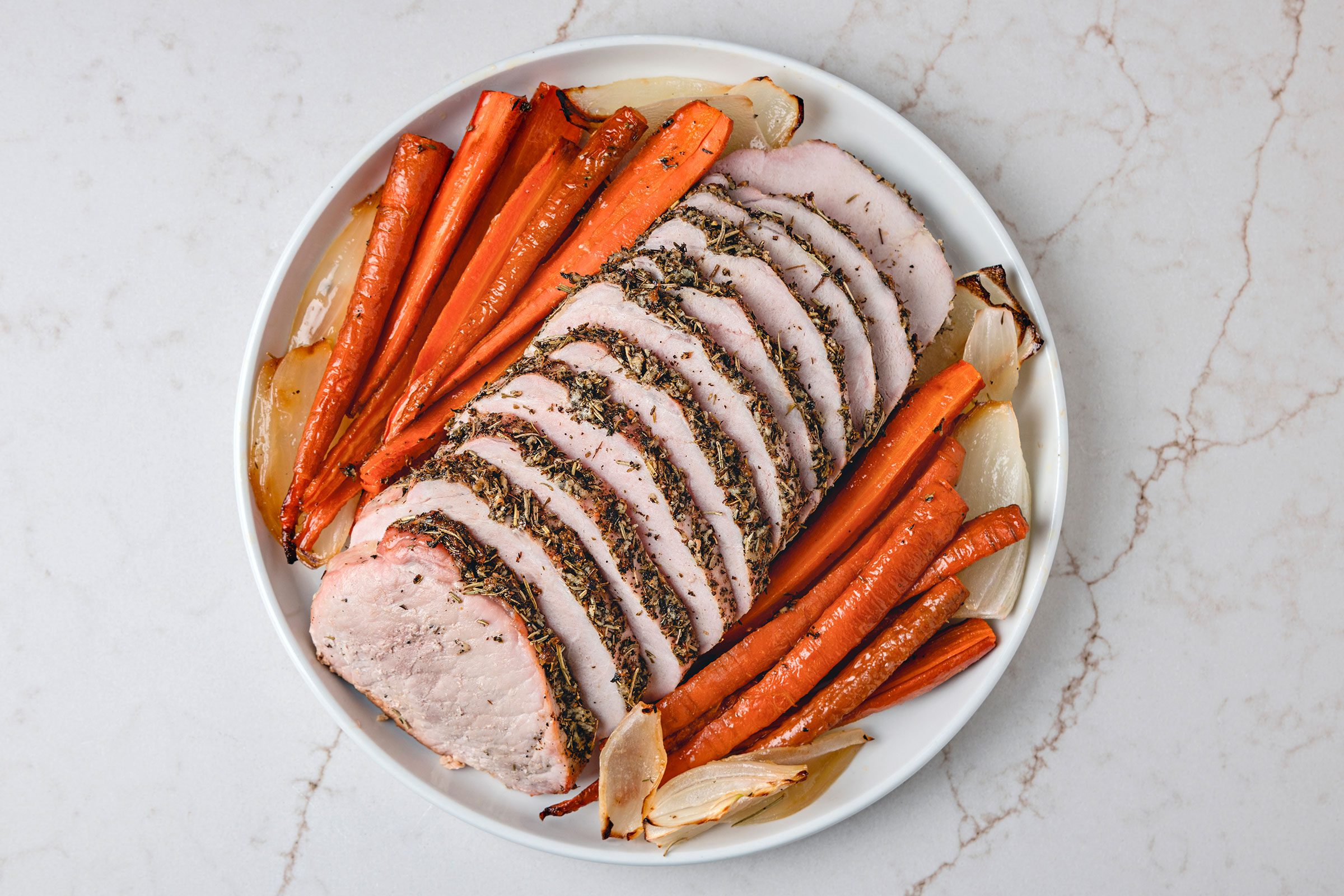 Italian Pork Loin sliced and served on a white plate with vegetables on side