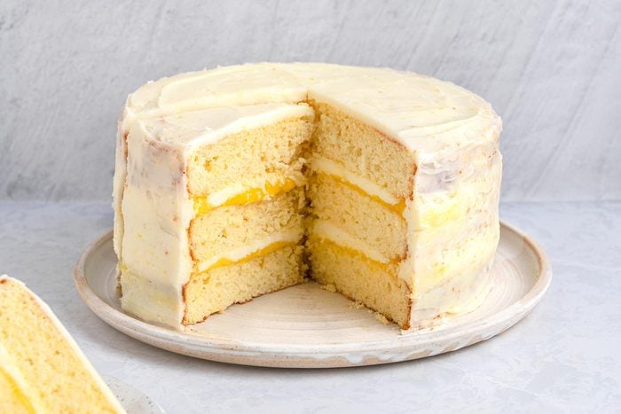 Wide shot of Lemon Curd cake with a slice taken out kept on top of a grey marbletop.
