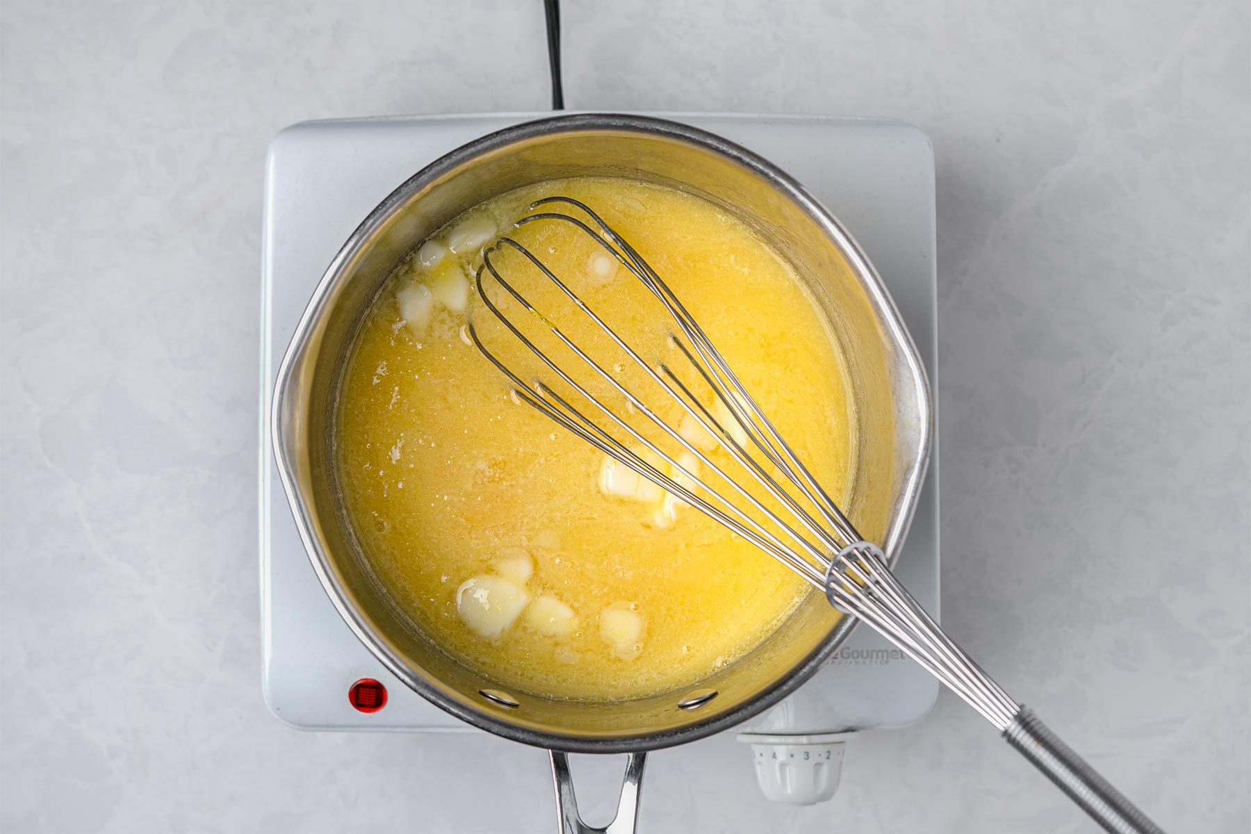 Melt butter in a saucepan kept on top of a grey marbletop.