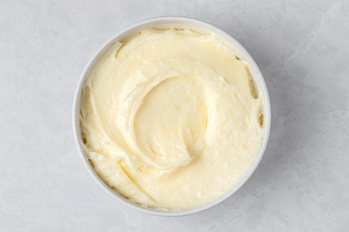 In a large bowl, beat cream cheese and butter kept on top of a grey marbletop.
