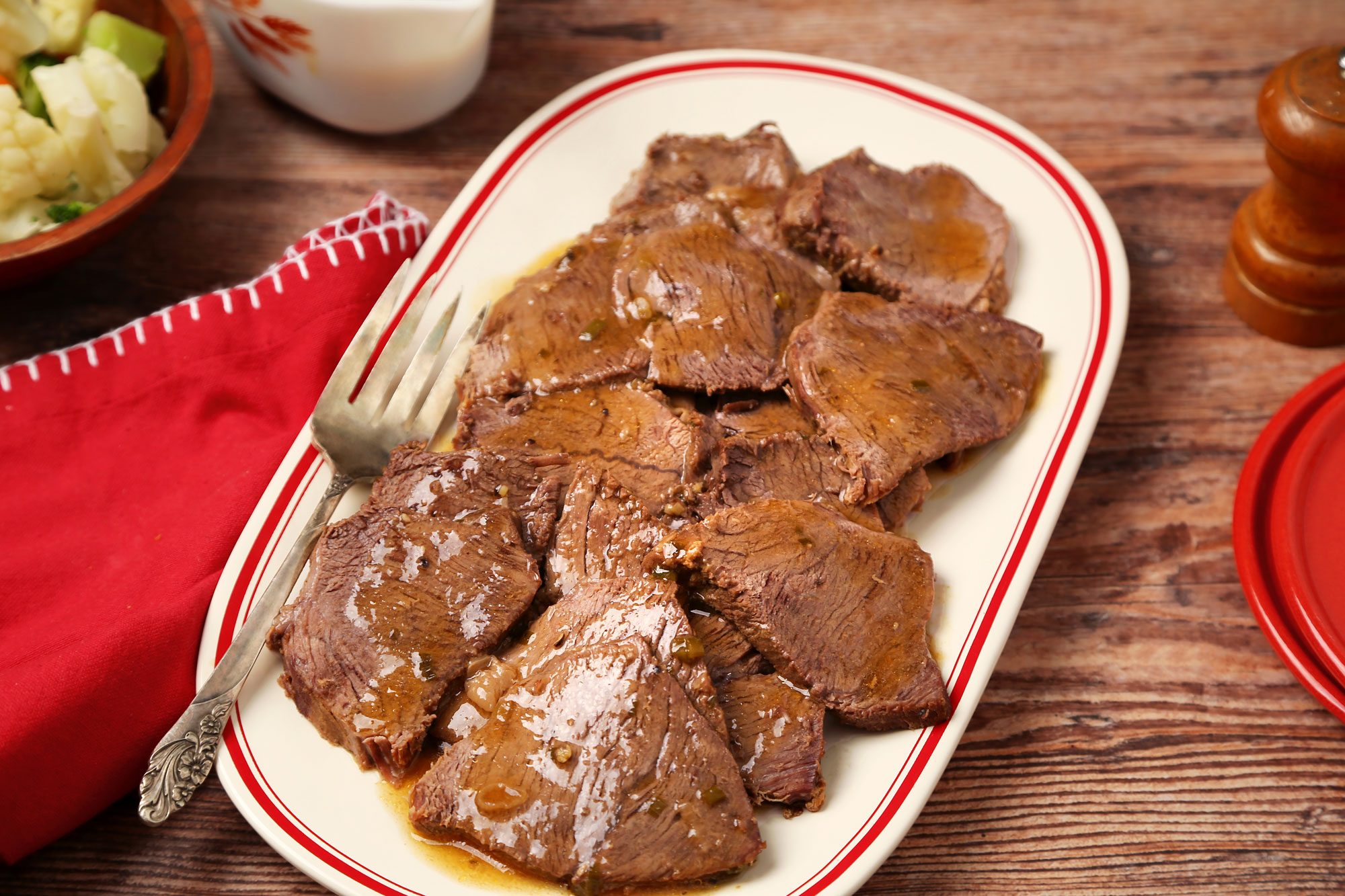 Marinated Pot Roast shot on a brown wooden surface. Sliced pot roast served on a platter with sauce