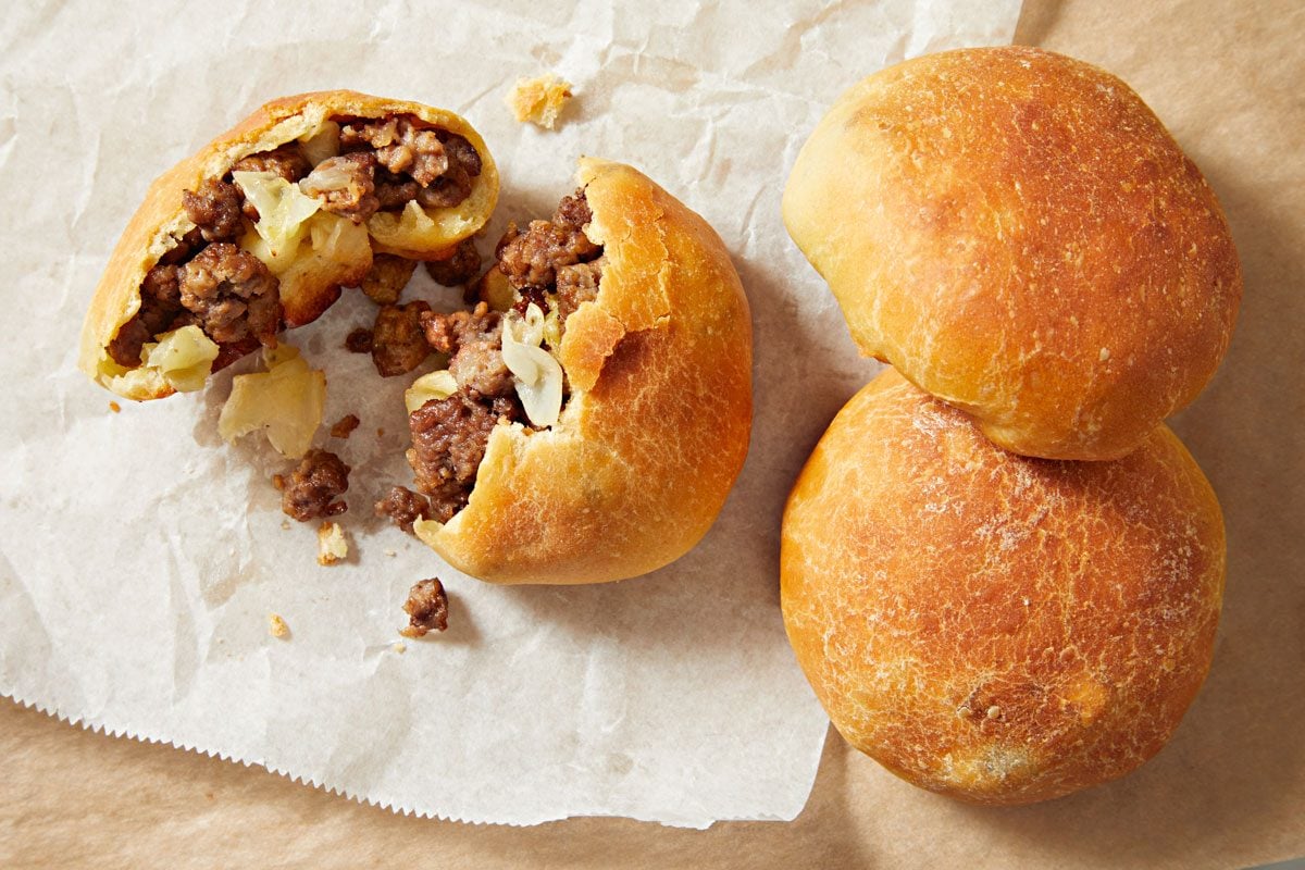 overhead shot of meat buns; several golden brown buns resting on a piece of parchment paper, with one bun partially opened to reveal its filling;