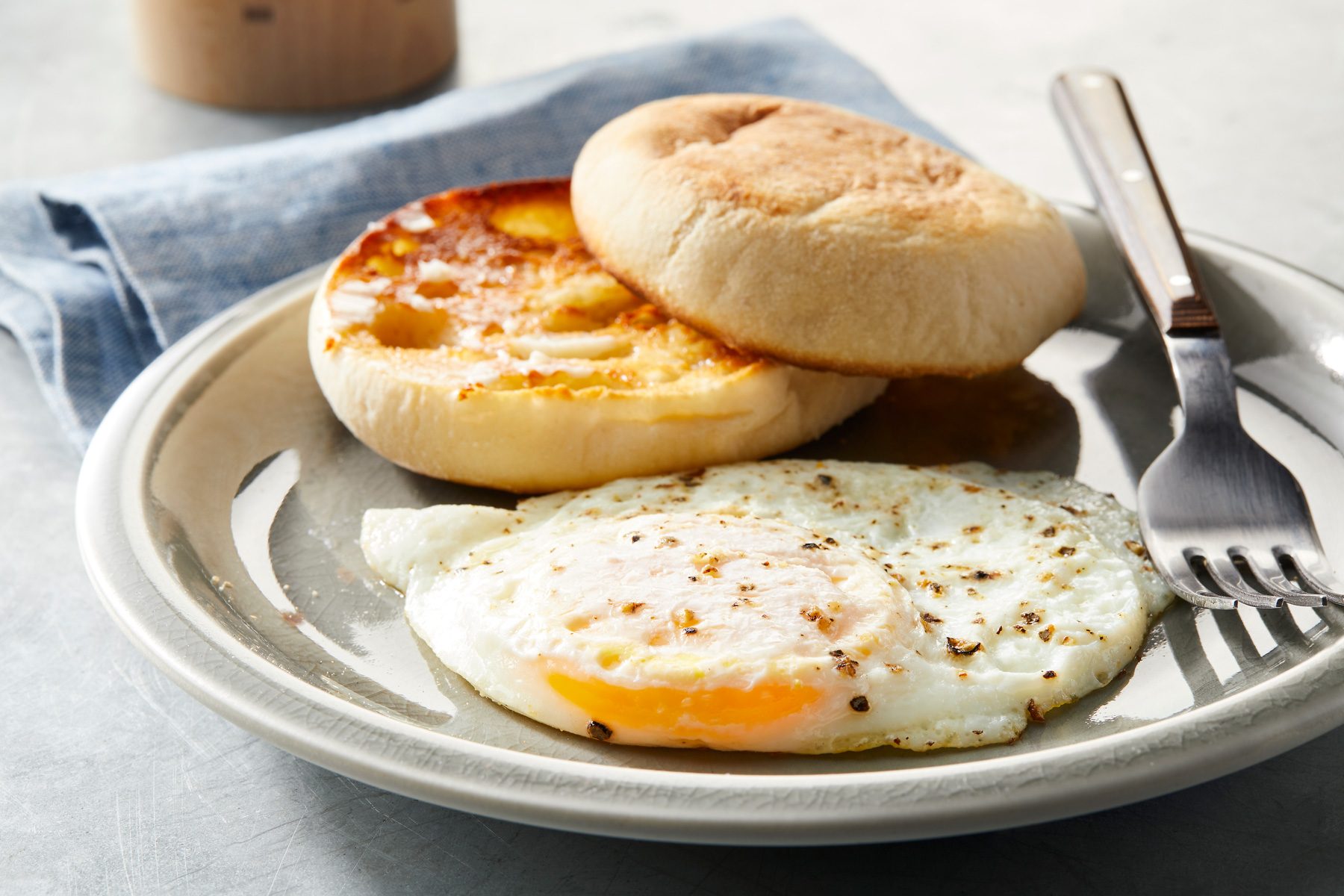 Close shot of Over-Easy Eggs; serve hot on a plate with bun and fork; over blue napkin; on grey surface;