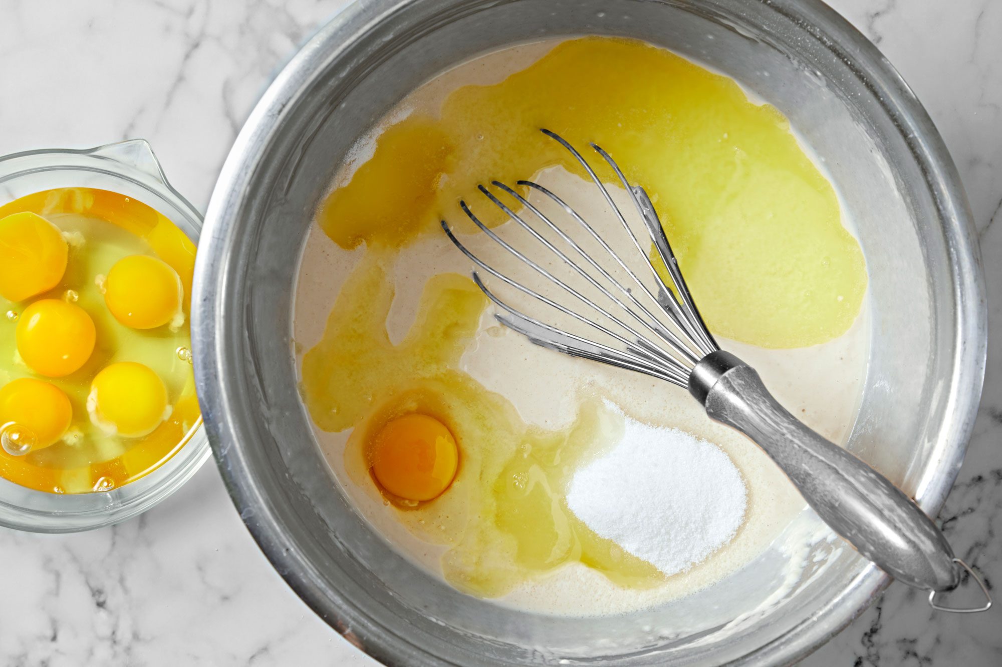 Overhead shot of add eggs; butter; salt and remaining 1/3 cup sugar; mix well; whisk tool; marble surface;