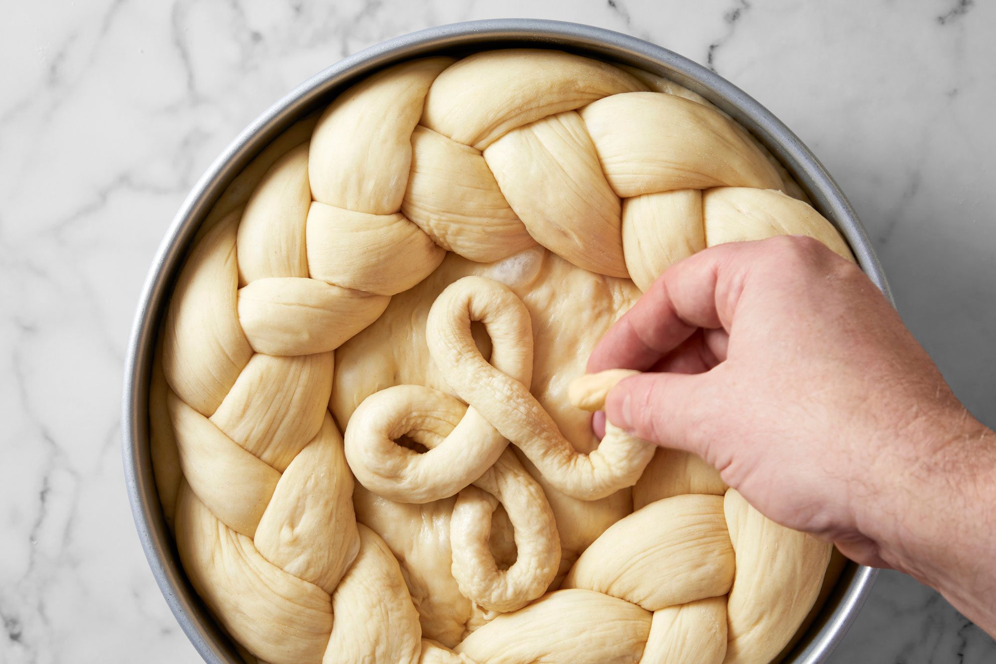 Overhead shot of shape scraps into 2 long thin ropes; form into rosettes or crosses; place 1 decoration on the center of each loaf; cover and let rise until doubled about 1 hour; marble surface