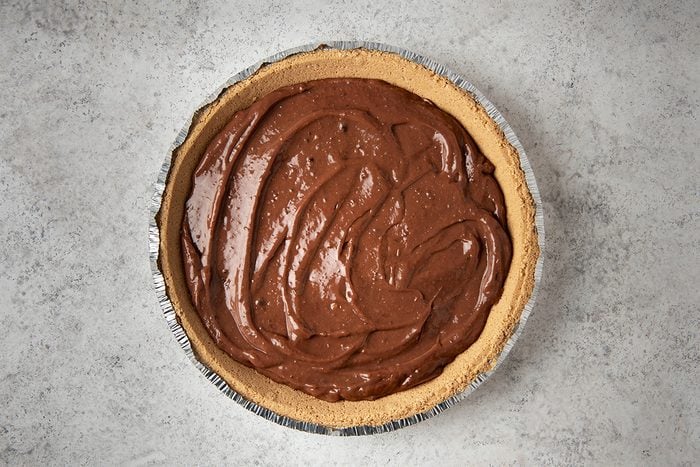 A chocolate cream pie with a smooth, rich filling sits in a metal pie tin. The crust is light brown and evenly browned, contrasting with the dark, glossy chocolate filling. The surface of the pie is textured with swirls.