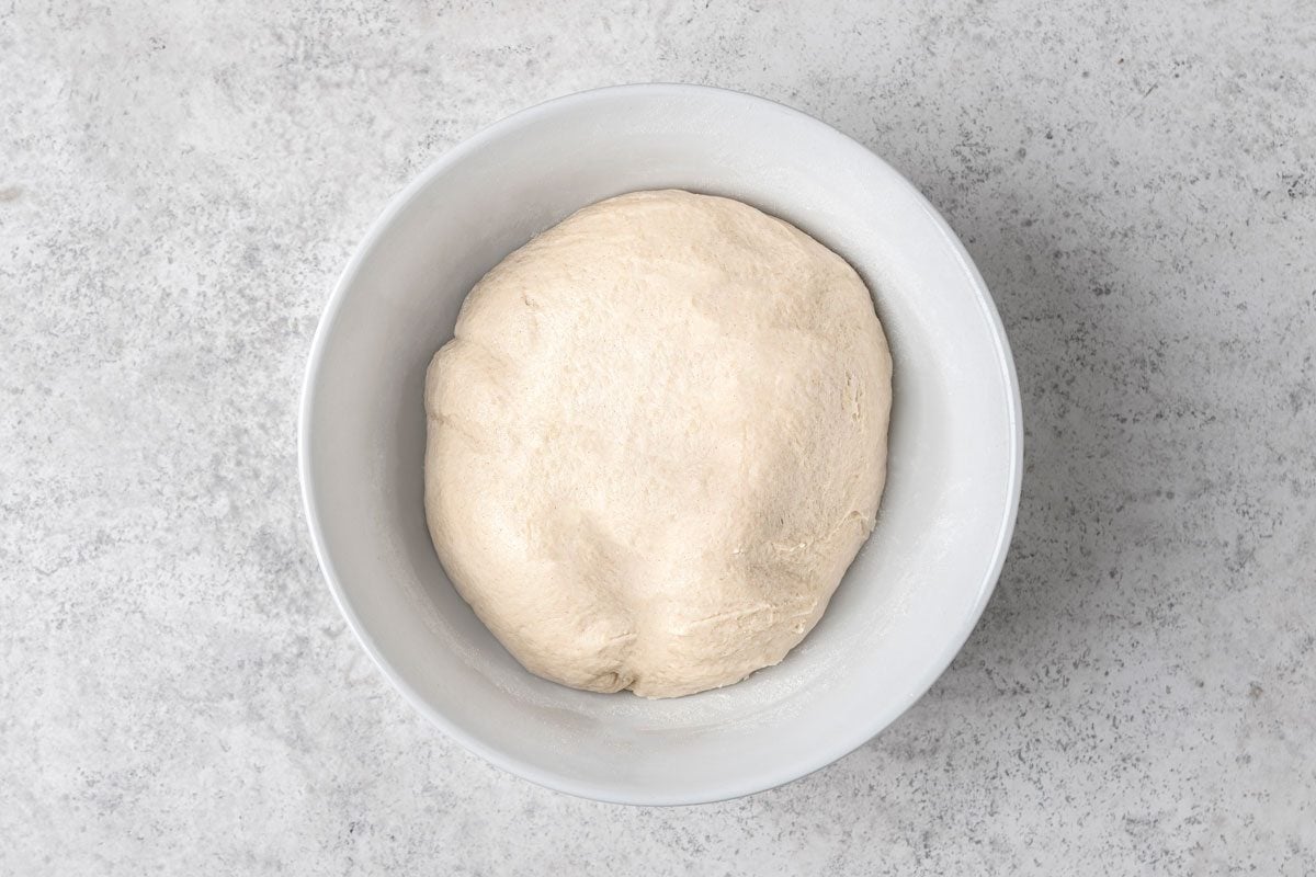 overhead shot of a ball of dough resting in a white oval shaped bowl, and is placed on a mottled grey surface
