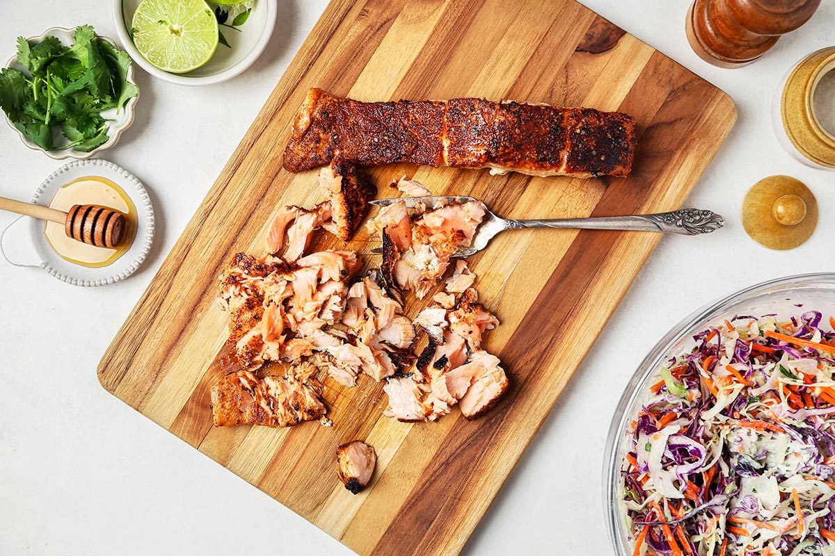 Cooked salmon being flaked on a wooden cutting board.