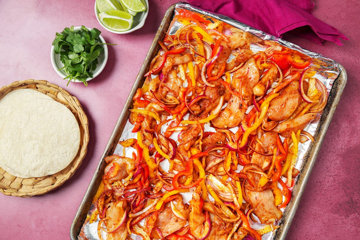 Chicken and peppers arranged on a baking sheet.