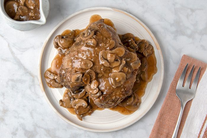 A plate of Salisbury steak covered in mushroom gravy, sitting on a marble surface. A napkin with a fork and knife is placed beside the plate.