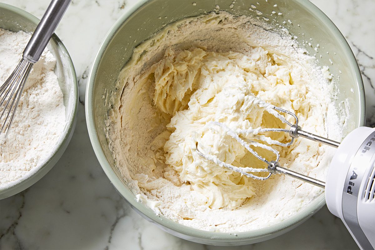 Overhead view of beating the cookie dough with an electric whisk in a large bowl. Next to it is a smaller bowl containing the dry ingredients.