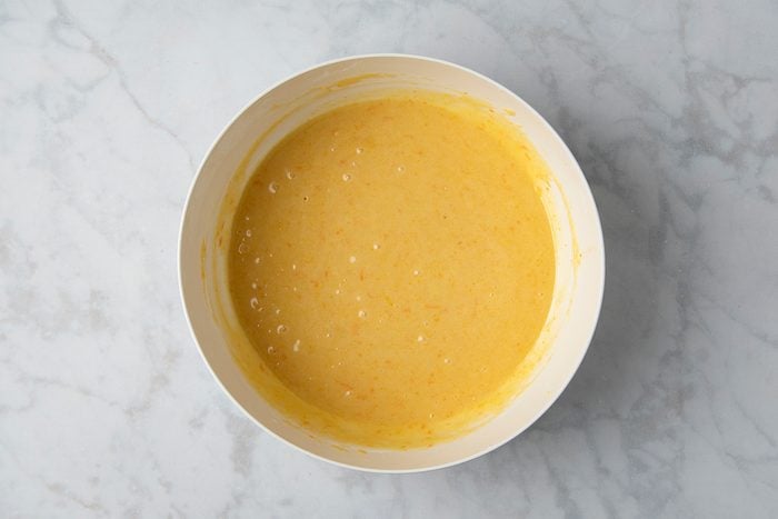 A white bowl filled with creamy yellow batter rests on a light marble surface.