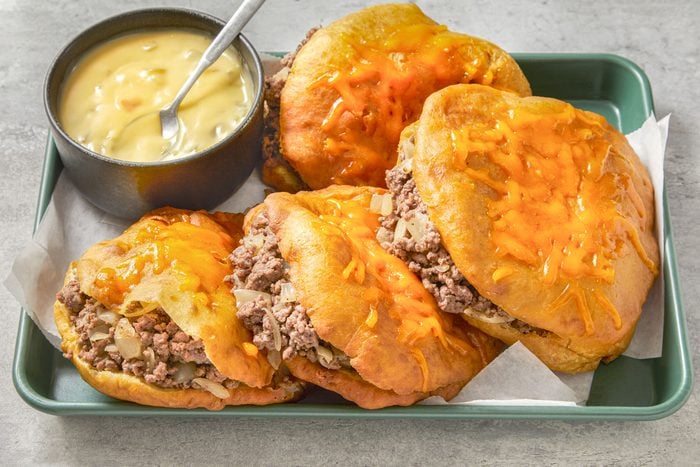 Table view shot of Beef-Stuffed Sopapillas; placed in a tray; top with cheese and serve with sauce; spoon; marble surface