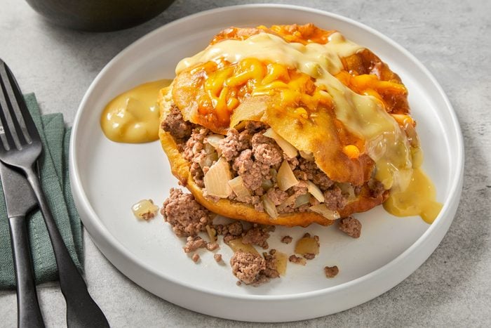 Close shot of Beef-Stuffed Sopapillas; top with cheese and serve on a plate with sauce; fork and knife; napkin, marble surface