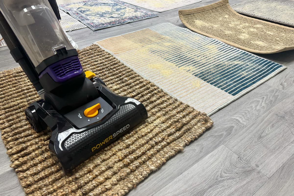 A vacuum cleaner cleaning one of several rugs placed on the floor.