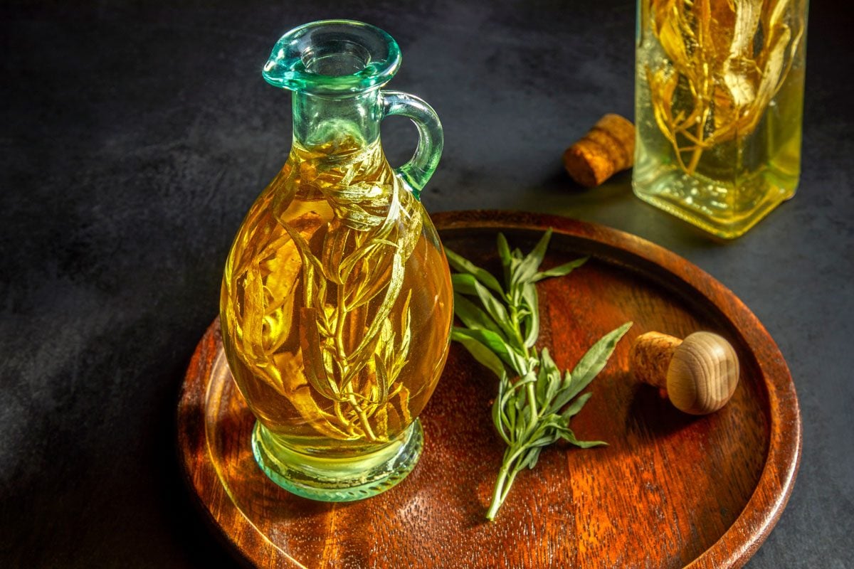 High angle shot of Tarragon Vinegar; poured into sterilized decorative bottles with additional tarragon; one bottle is placed on a wooden tray with an open lid; and while another placed on a dark surface;