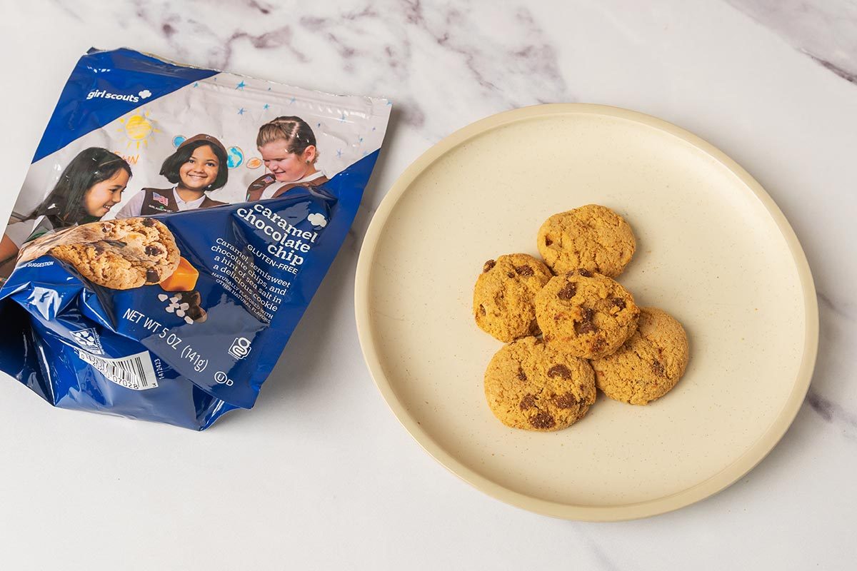 Package of caramel chocolate chip Girl Scout Cookies next to several cookies on a plate