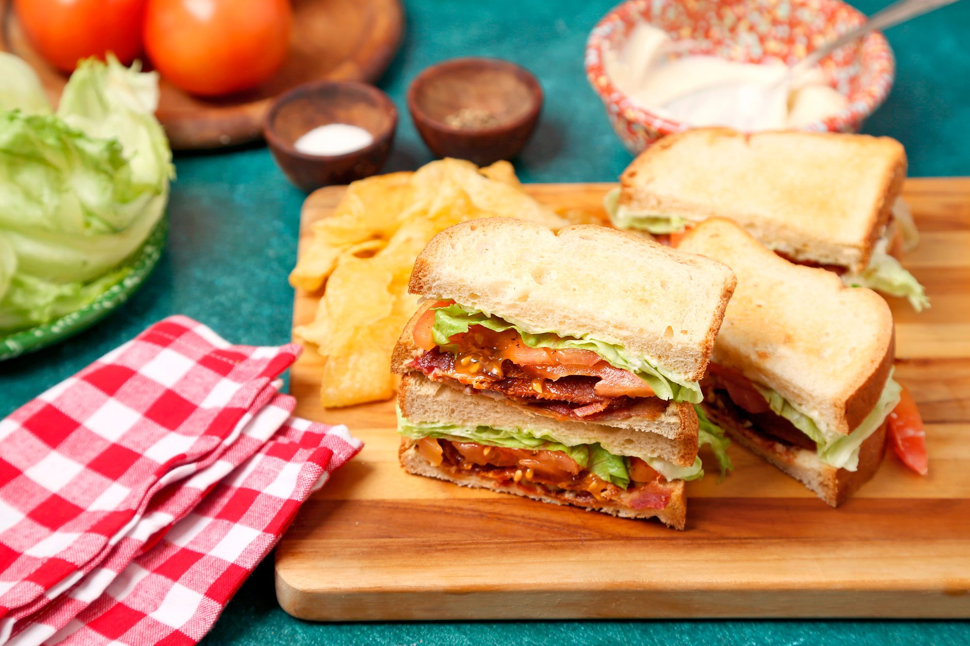 Cover pull push image of Taste of Home's BLT shot on a blue green surface. Assembled BLT sliced and served on a wooden surface.