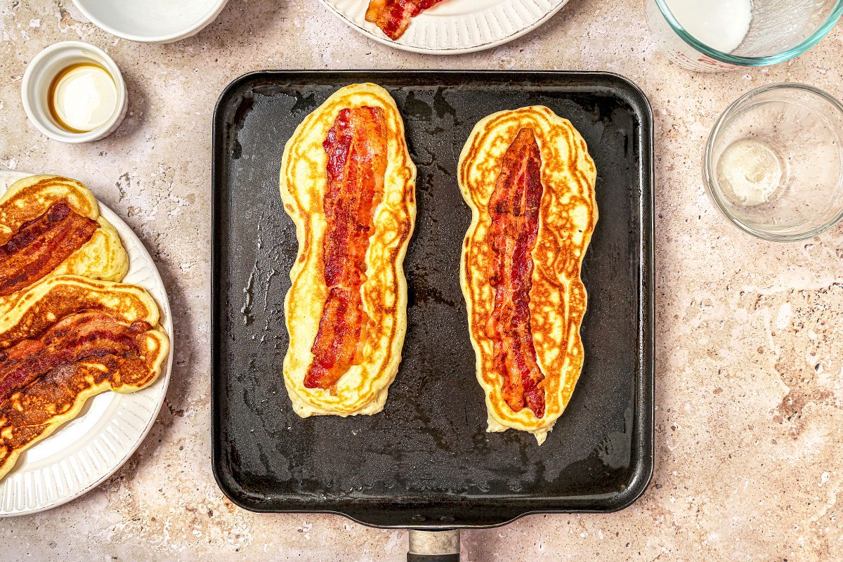 Pancakes being cooked in a griddle pan with bacon
