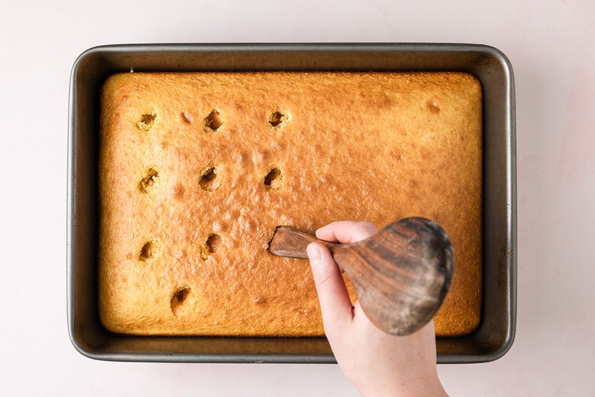 Boston Cream Poke Cake overhead shot of poked holes in cake with hand and spoon
