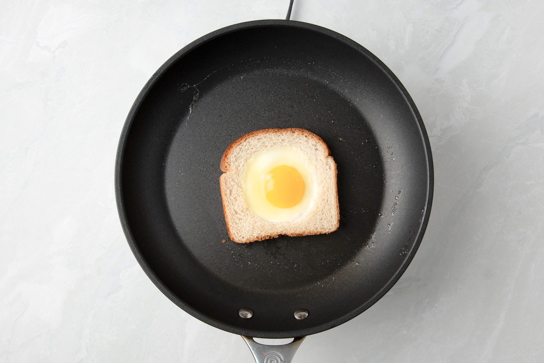 Overhead shot of place egg in the hole; cook over medium heat until the bread is lightly browned about 2 minutes; on marble surface;