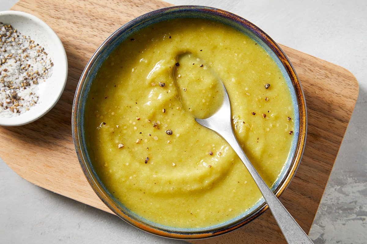 Close-ip shot of Green Enchilada Sauce; served in a bowl; placed over wooden tray with a spoon; all set on a marbel surface