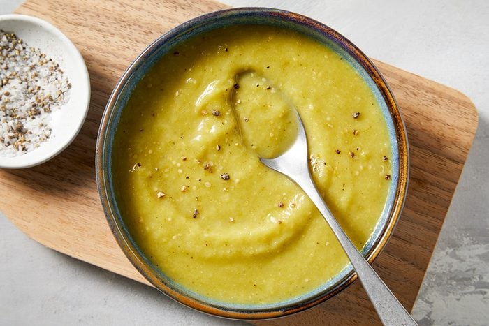 Close-ip shot of Green Enchilada Sauce; served in a bowl; placed over wooden tray with a spoon; all set on a marbel surface