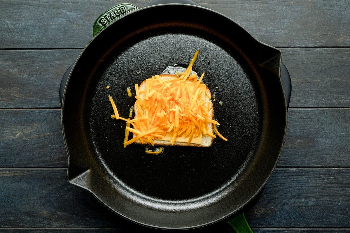 Place a slice of American cheese on bread and divide shredded cheddar cheese on top