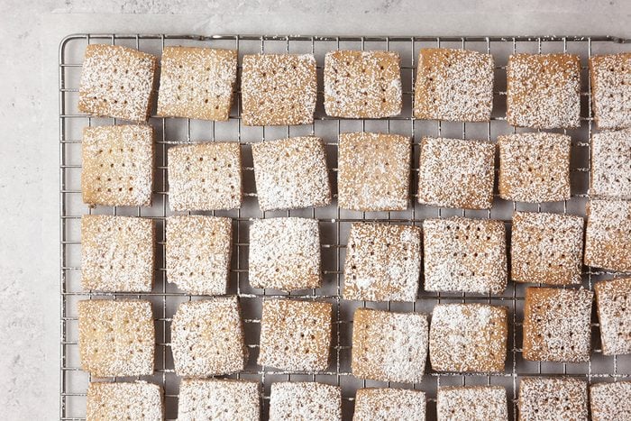 Square cookies with powdered sugar are arranged in rows on a wire cooling rack.