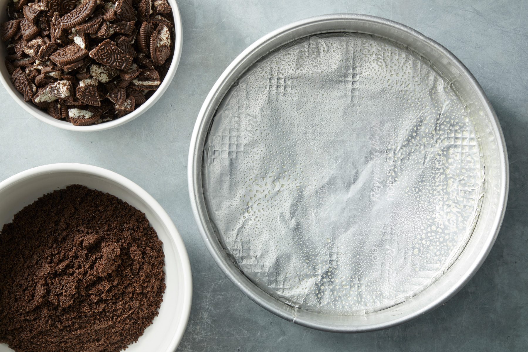 Overhead shot of a large bowl combine crushed cookies and butter; on a grey surface;